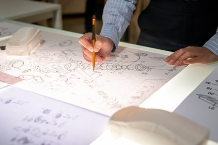 Close-up of unrecognizable female vehicle designer standing at table and drawing car component