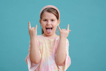 Portrait of funny little girl showing her tongue and posing at camera against the blue background