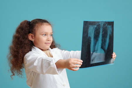 Little girl with curly hair examining x-ray image in her hands standing against the blue background
