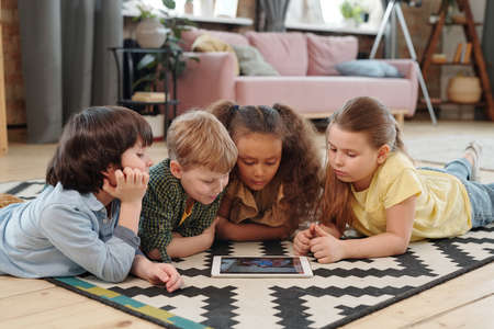 Group of children lying on the floor and watching cartoons together on digital tablet at home