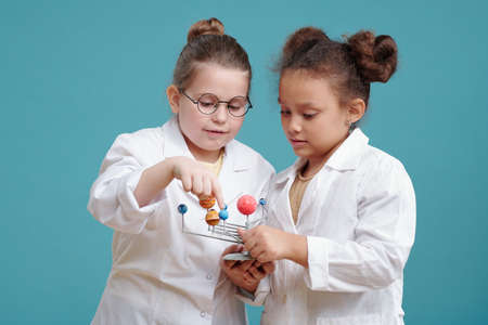 Two little chemists in white coats examining chemical formula together against the blue background