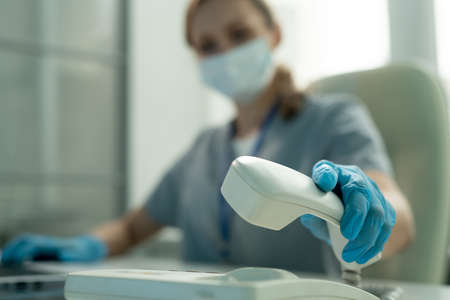Close-up of lab worker in blue gloves picking up phone while answering call in office
