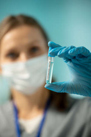 Close-up of female nurse in blue glove holding test tube of coronavirus vaccine while preparing for...