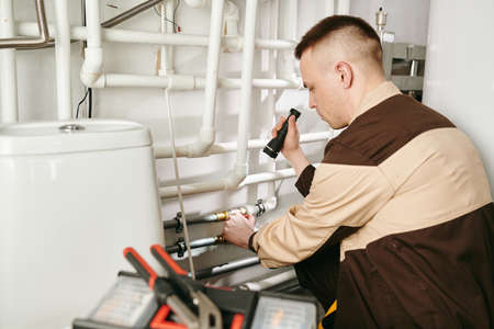 A man in uniform using handtool while repairing pipe in lavatory