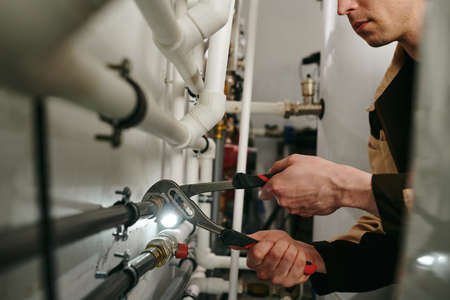 Repairman using a tool to fix parts of pipes during workの写真素材
