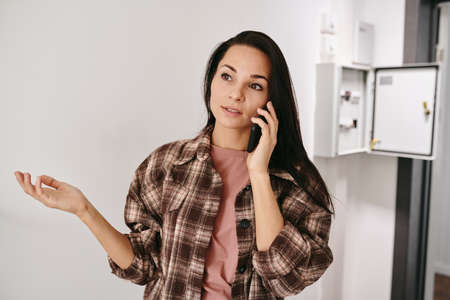Young brunette female explaining her problem on mobile phone while calling plumber
