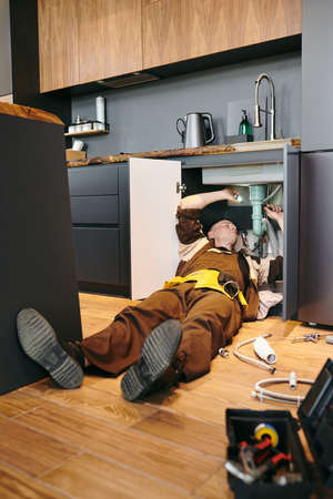 Young plumber lying on the floor while repairing kitchen sinkの写真素材