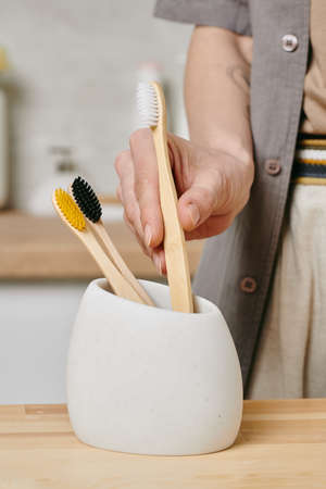 Young woman holding a toothbrush out of white cup in the morning