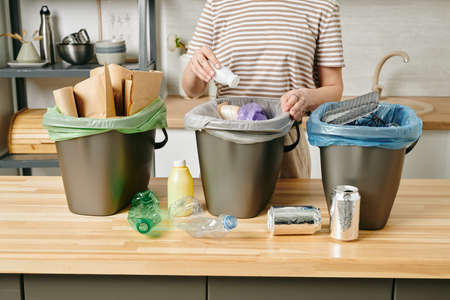 A person putting small plastic yoghurt bottle into kitchen trash bin