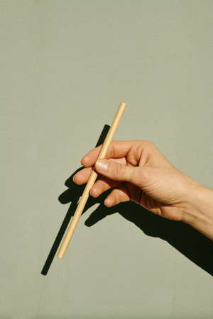 Hand of female holding stick in front of camera over grey wallの写真素材