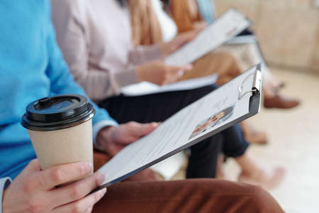 Close-up of unrecognizable job candidate holding CV and drinking coffee while waiting for interview in lineの写真素材
