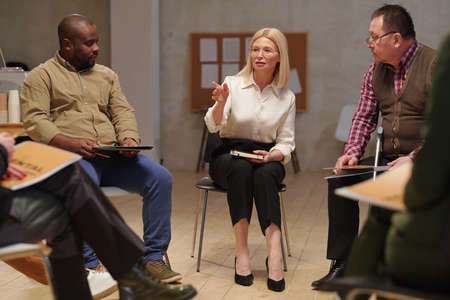 Mature psychologist talking to group of people during session