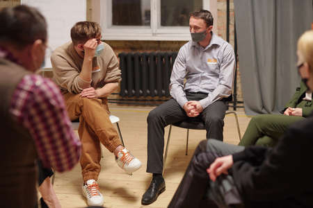 People in protective masks sitting in circle and describing their problems during session