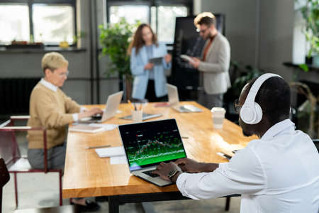 African businessman in headphones working with online data against colleagues