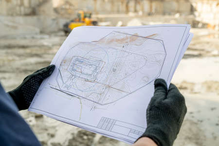 Gloved hands of builder holding paper with sketch of constructionの写真素材