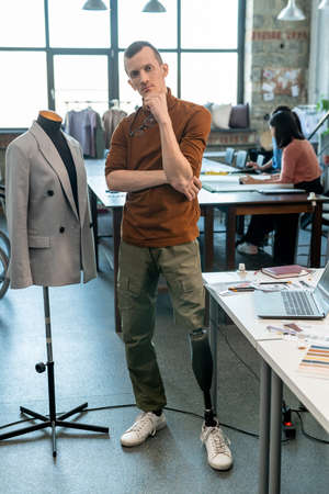 Disable male designer in casualwear standing by workplace against female colleaguesの写真素材