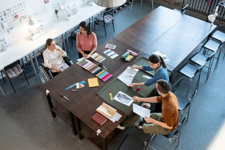Two small groups of fashion designers working by large table in modern workshopの写真素材