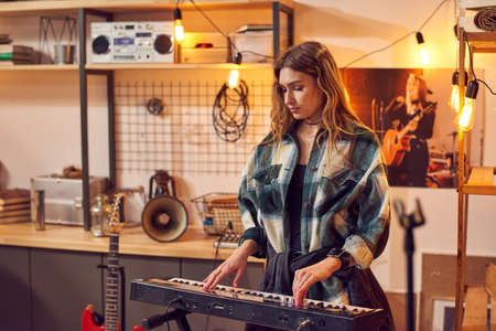 Blond girl playing keyboard in studio of music recording