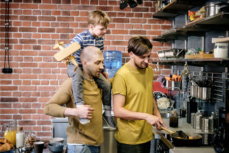 Two happy gay men and little boy cooking in kitchen environmentの写真素材