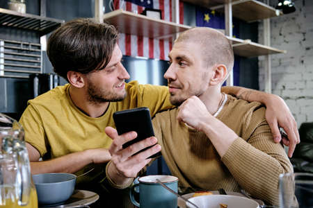 Young male embracing his boyfriend during talk by breakfastの写真素材