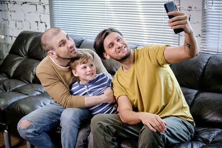 Two young men and cute boy looking at smartphone screen in living-roomの写真素材