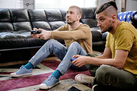 Two guys with joysticks playing video game on the floor of living-roomの写真素材