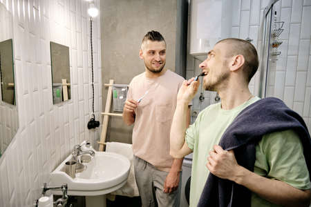 Two young gay men brushing teeth in bathroom in the morningの写真素材