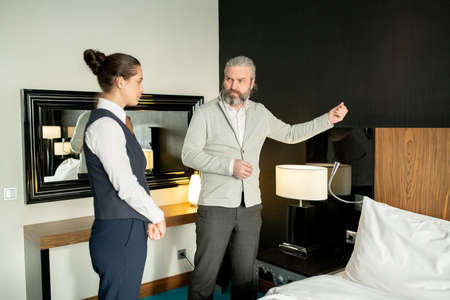 Mature man complaining housekeeping manager about neighbours in hotel roomの写真素材