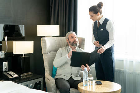 Young hotel manager offering menu to mature businessman