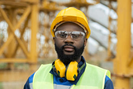 Young African engineer in workwear and protective helmet looking at you