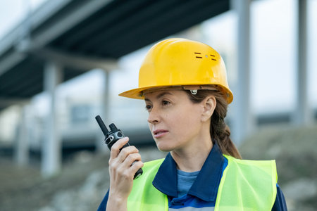 Female inspector or engineer using walkie-talkie while working on construction siteの写真素材