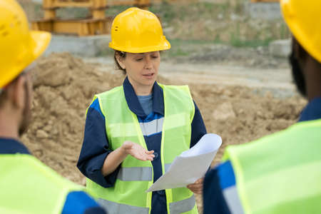 Contemporary engineer with paper standing in front of intercultural male colleagues during...