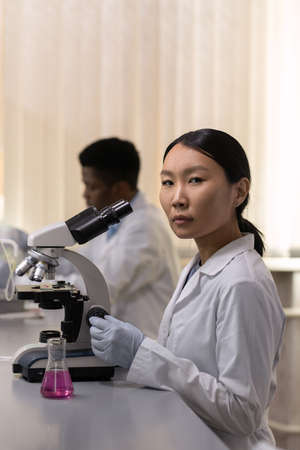 Young serious woman in lab coat and gloves working in scientific laboratory