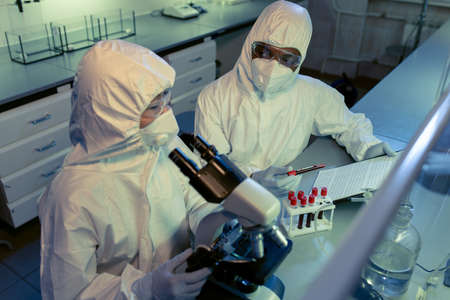 Two intercultural scientists in coveralls consulting about working data on paper