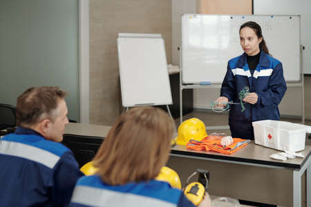 Female occupational safety instructor in blue jacket standing at table and holding oxygen mask while explaining how to give first aidの写真素材