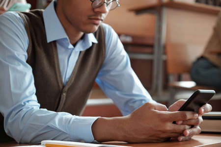 Hands of mixed-race guy with smartphone sitting by desk
