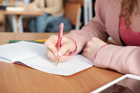 Hands of female student making notes in copybook during lecture