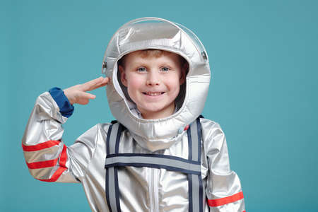 Happy cute little boy in space-suit keeping hand by temple