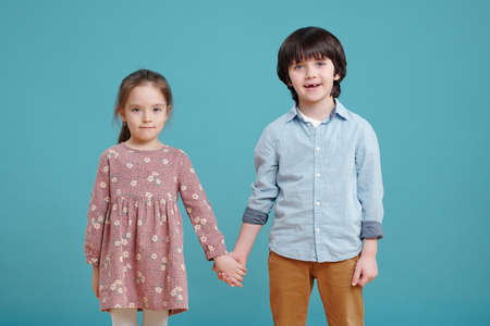 Adorable little boy and girl holding by hands and looking at youの写真素材