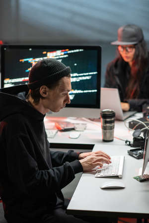Male hacker typing in front of computer in office