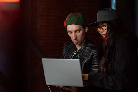 Two young hackers with laptop decoding information in the darkの写真素材