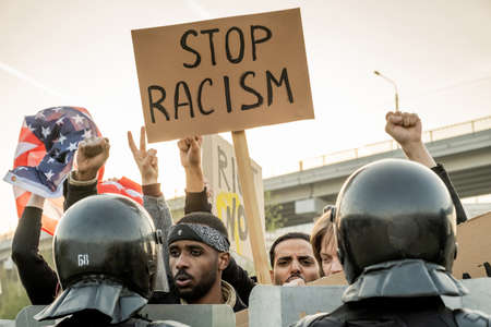 Group of displeased young American people raising fists and banner while asking to stop racism,...