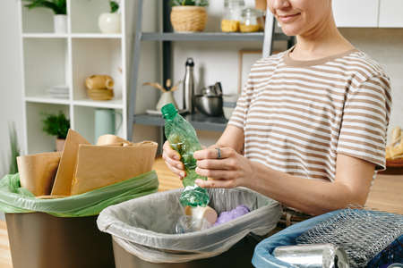 Young female smashing plastic bottle over one of three trash binsの写真素材