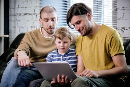 Two fathers and their preteen son spending time together at home and watching movie or playing game...