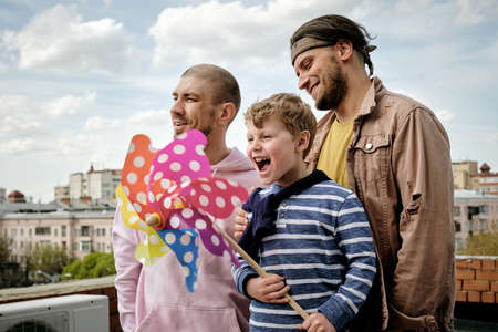 Happy young people and little boy standing on rooftop of building with rainbow pinwheel in hands