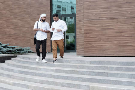 Serious young Muslim men in white shirts discussing new project while leaving officeの写真素材