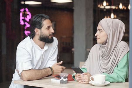 Young Muslim friends standing at counter table and chatting while meeting in cafeの写真素材