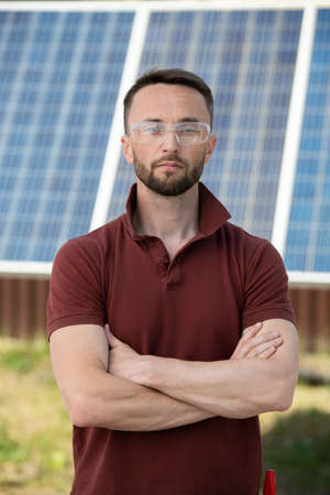 Serious man in protective googles standing against photovoltaic panel he installed in backyard of his houseの写真素材