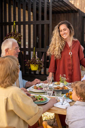 Pretty smiling young woman at dinner party with her friends and family members