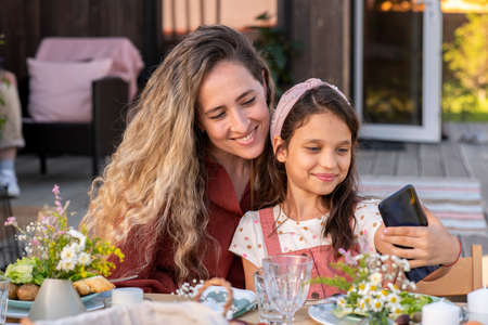 Beautiful young woman photographing with her adorable preteen daughter at family dinner